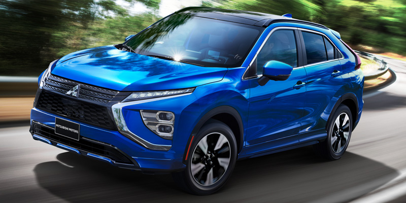 Latest 2026 Mitsubishi SUV in vibrant blue driving on a winding road, featuring a sleek modern design, black accents, and a motion-blurred green landscape background.